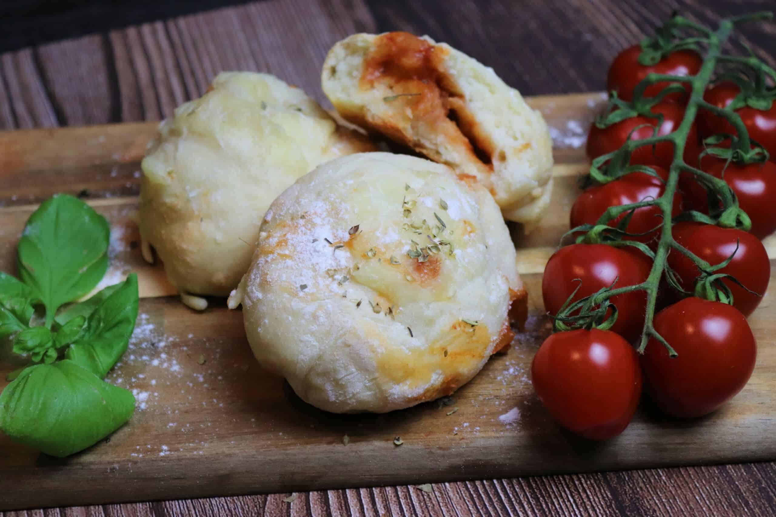 Gefüllte Pizzabrötchen mit frischen Tomaten und ein paar Basilikumblättern auf einem Holzbrett serviert.